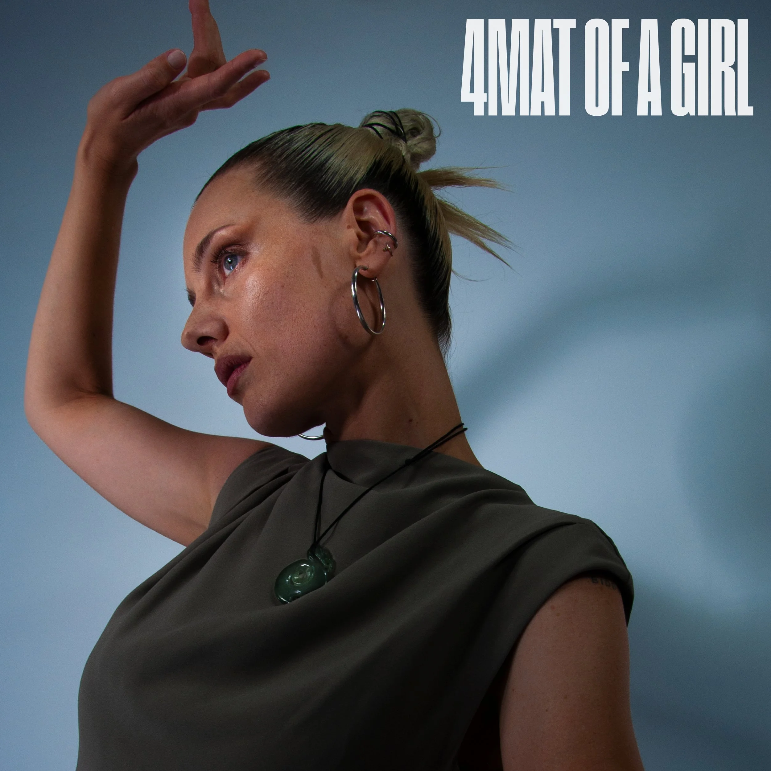 Close-up of artist profile with her arm raised, showing her face, hair, and multiple earrings, against a plain background, with large white text that reads '4MAT OF A GIRL'.