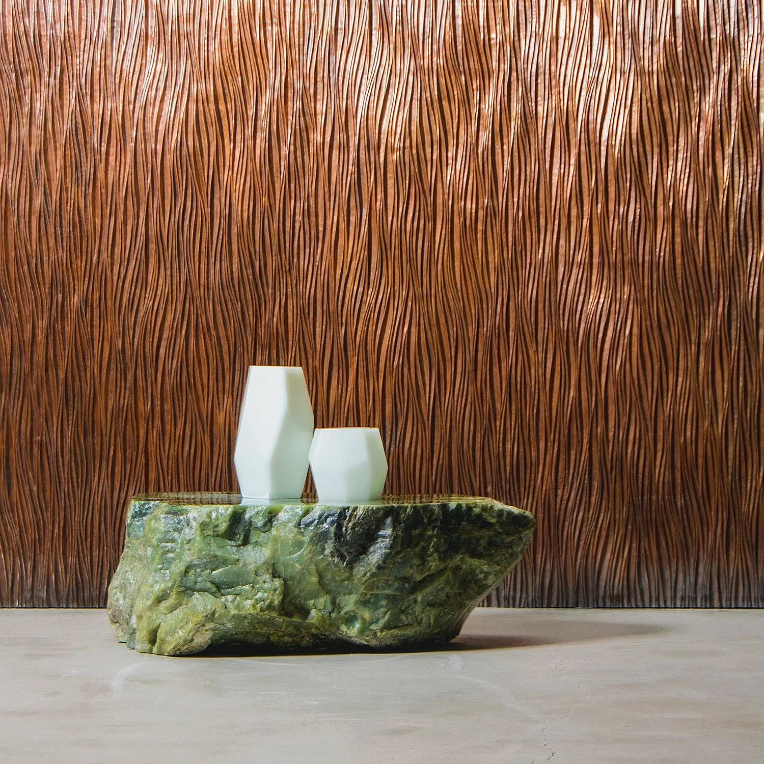 Two white vases, one tall and one short, placed on a green, textured stone table against a brown textured wooden wall.