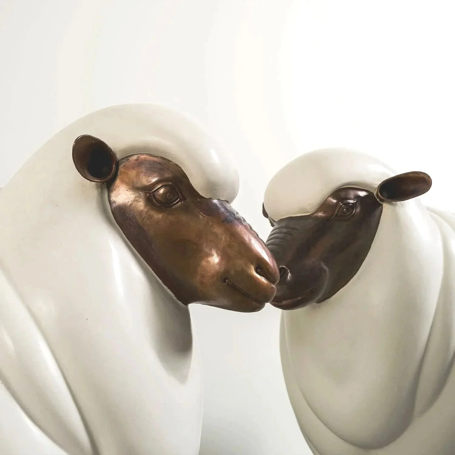 Close-up of two white ceramic sculptures of faces with bronze-colored metallic masks forming a mirror image, facing each other.
