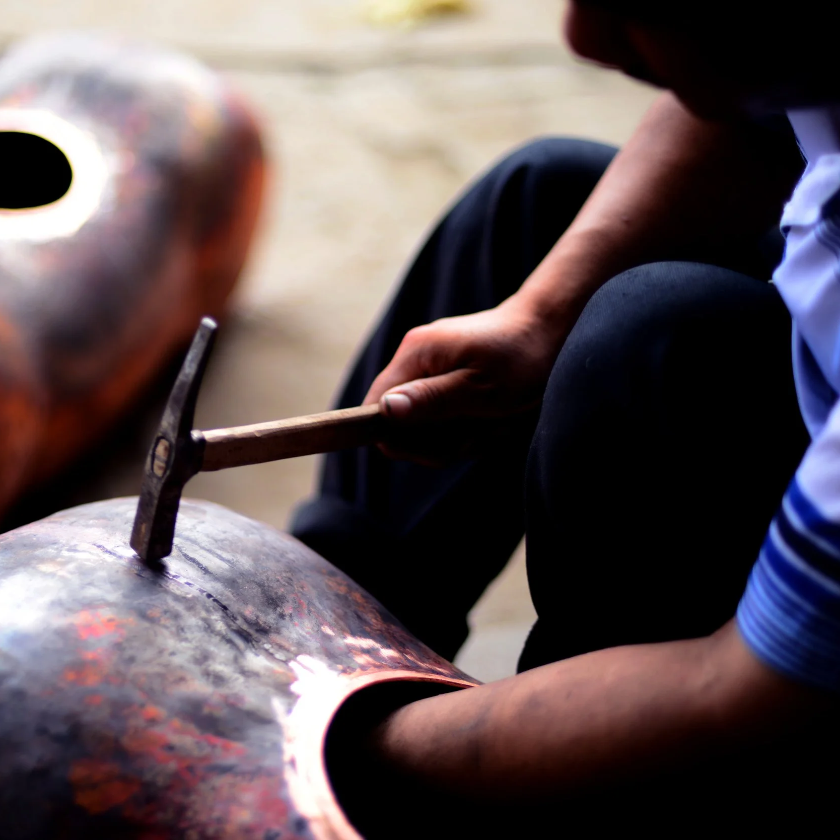 Person shaping a hot metal object with a hammer on an anvil.