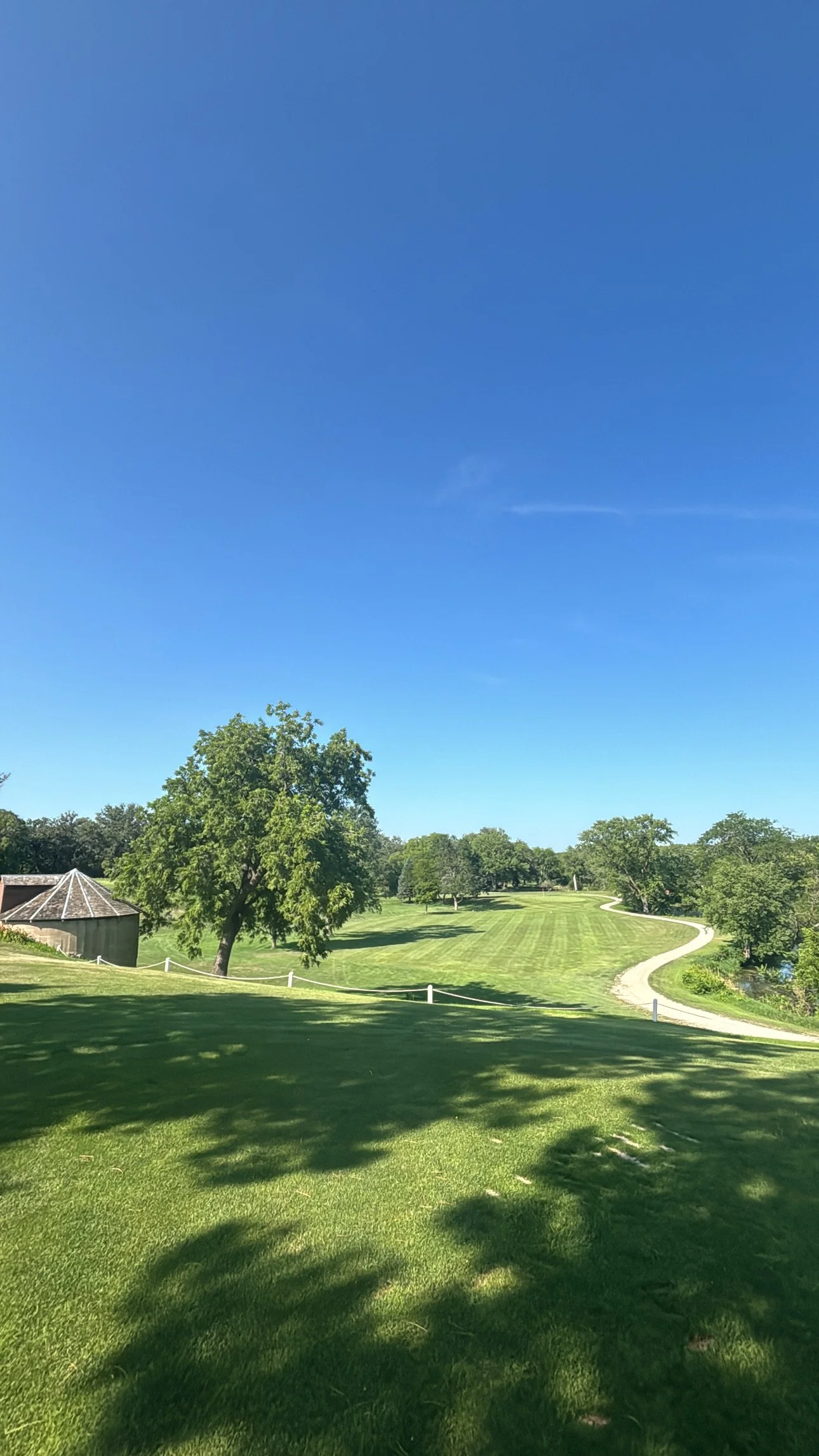 A scenic view of a golf course with green grass, trees, and a winding path under a clear blue sky.