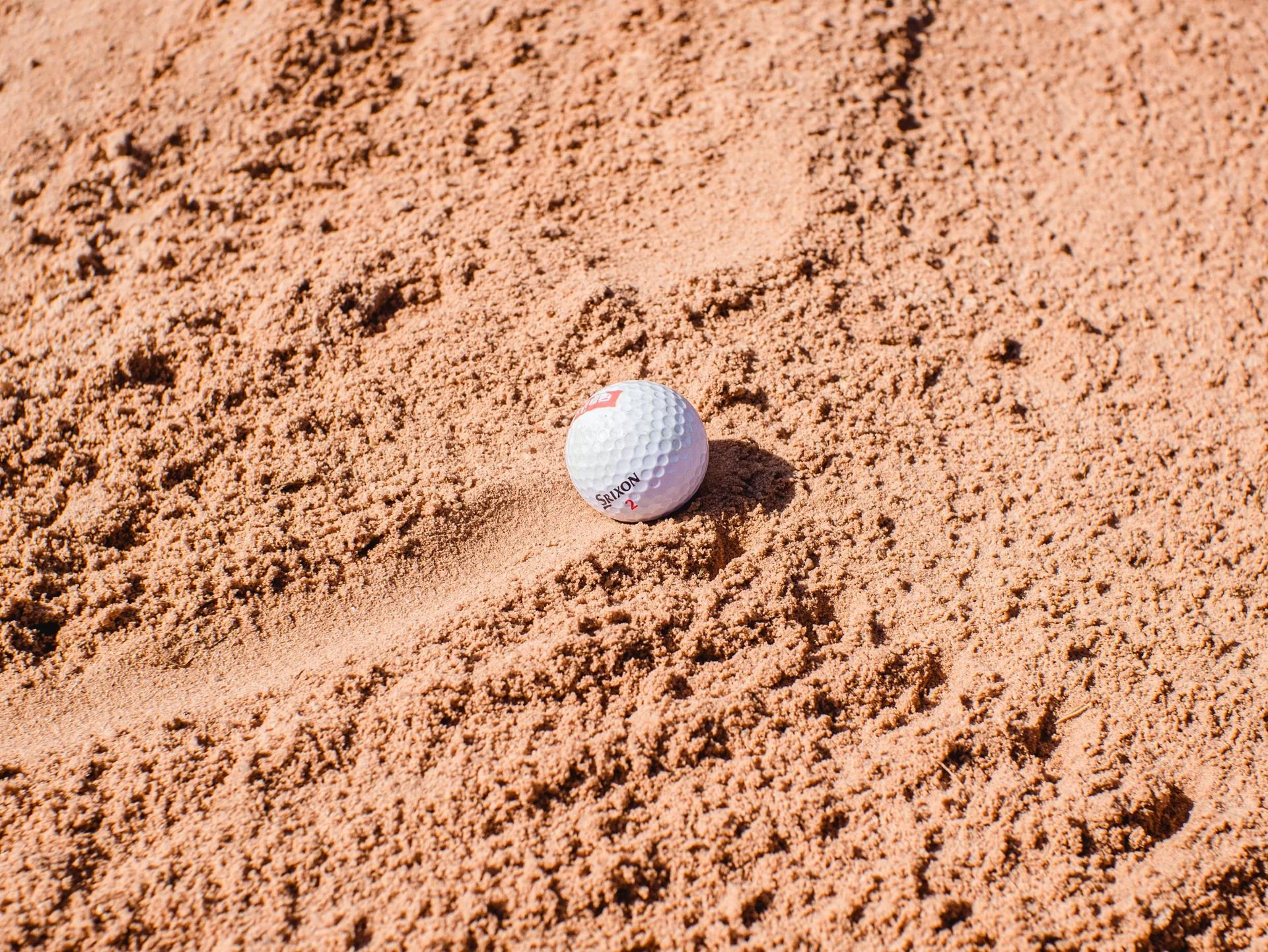 Close-up of a golf ball on a sand trap or bunker in a golf course.