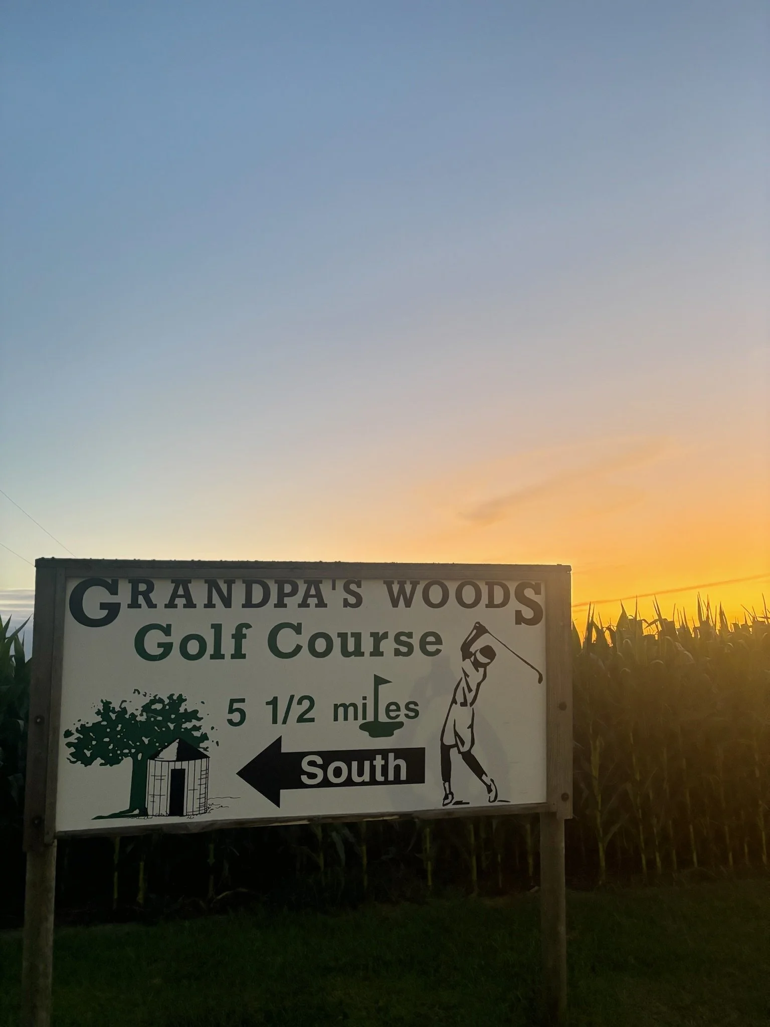 Sign pointing south to Grandpas Woods Golf Course, 5 1/2 miles away, with illustrations of a tree, a water tower, and a golfer.