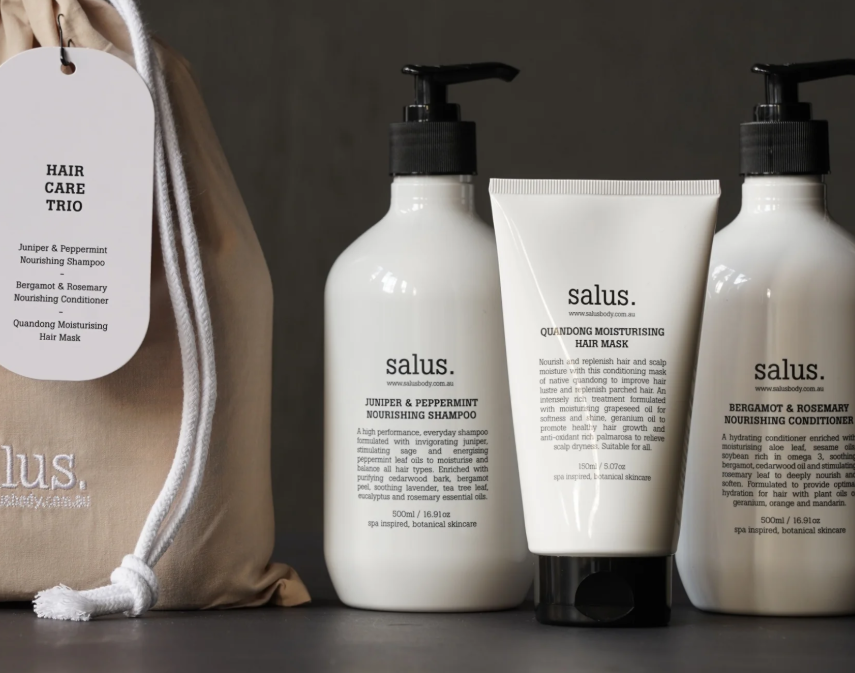 Three bottles of Salus hair care products and a cloth bag on a dark surface.