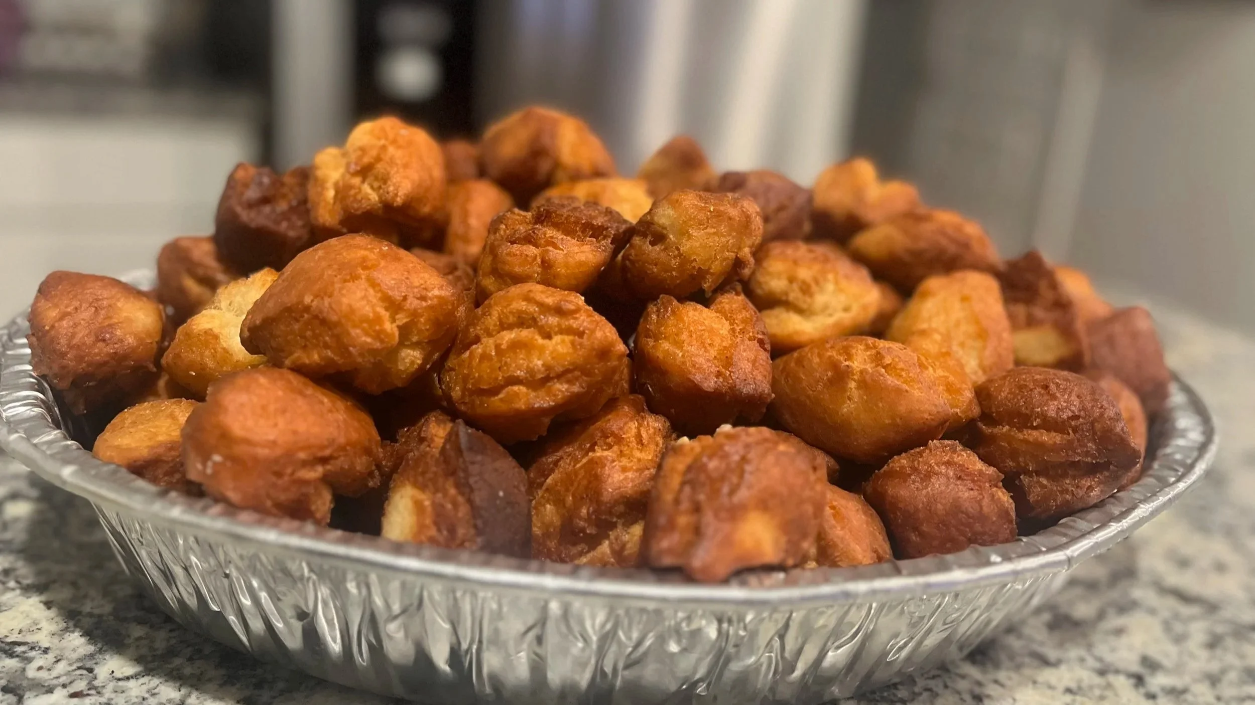 Close-up of a silver geometric bowl filled with fried chicken nuggets on a gray granite countertop.