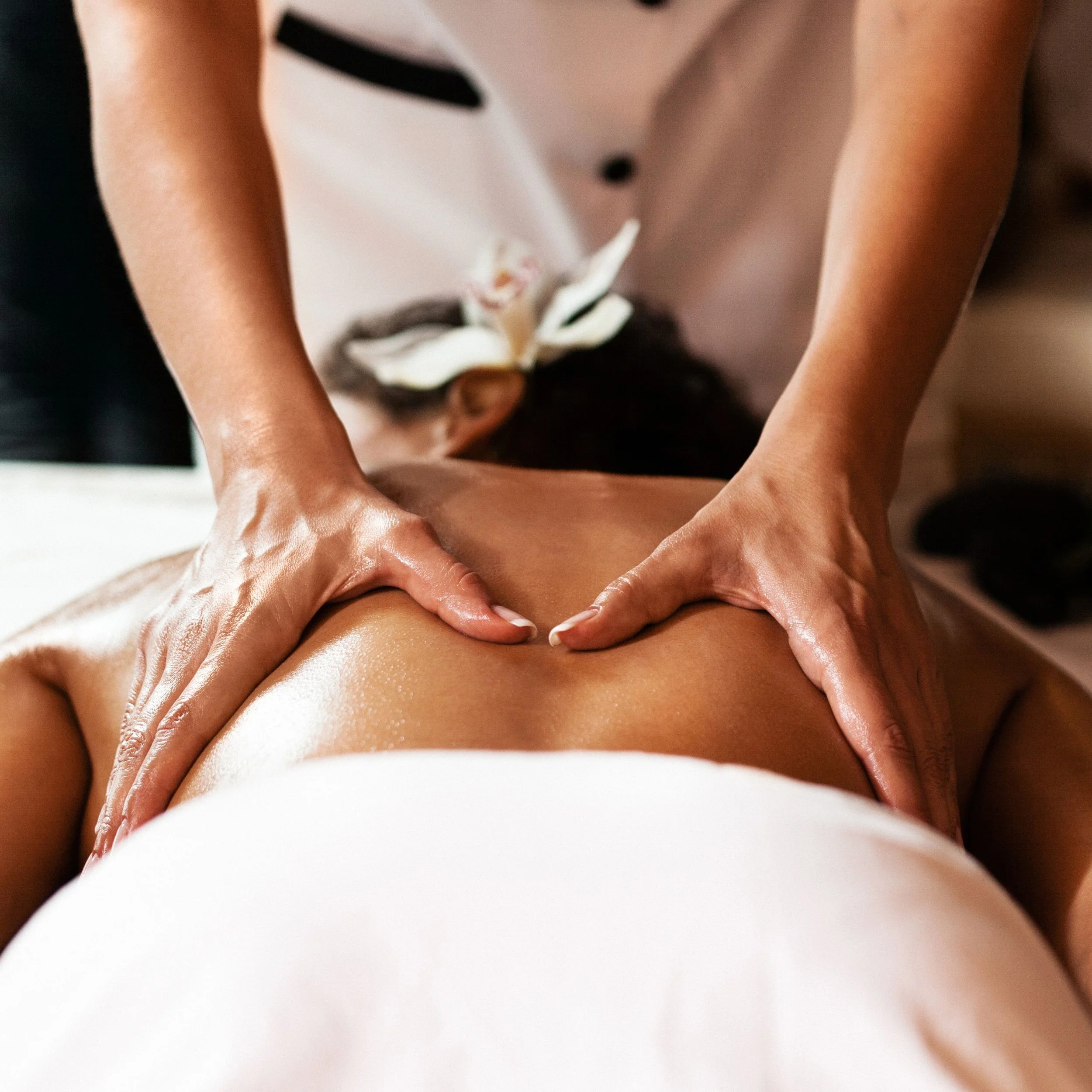 Close-up of a person receiving a massage, focusing on their back and hands, with a white flower in the background.
