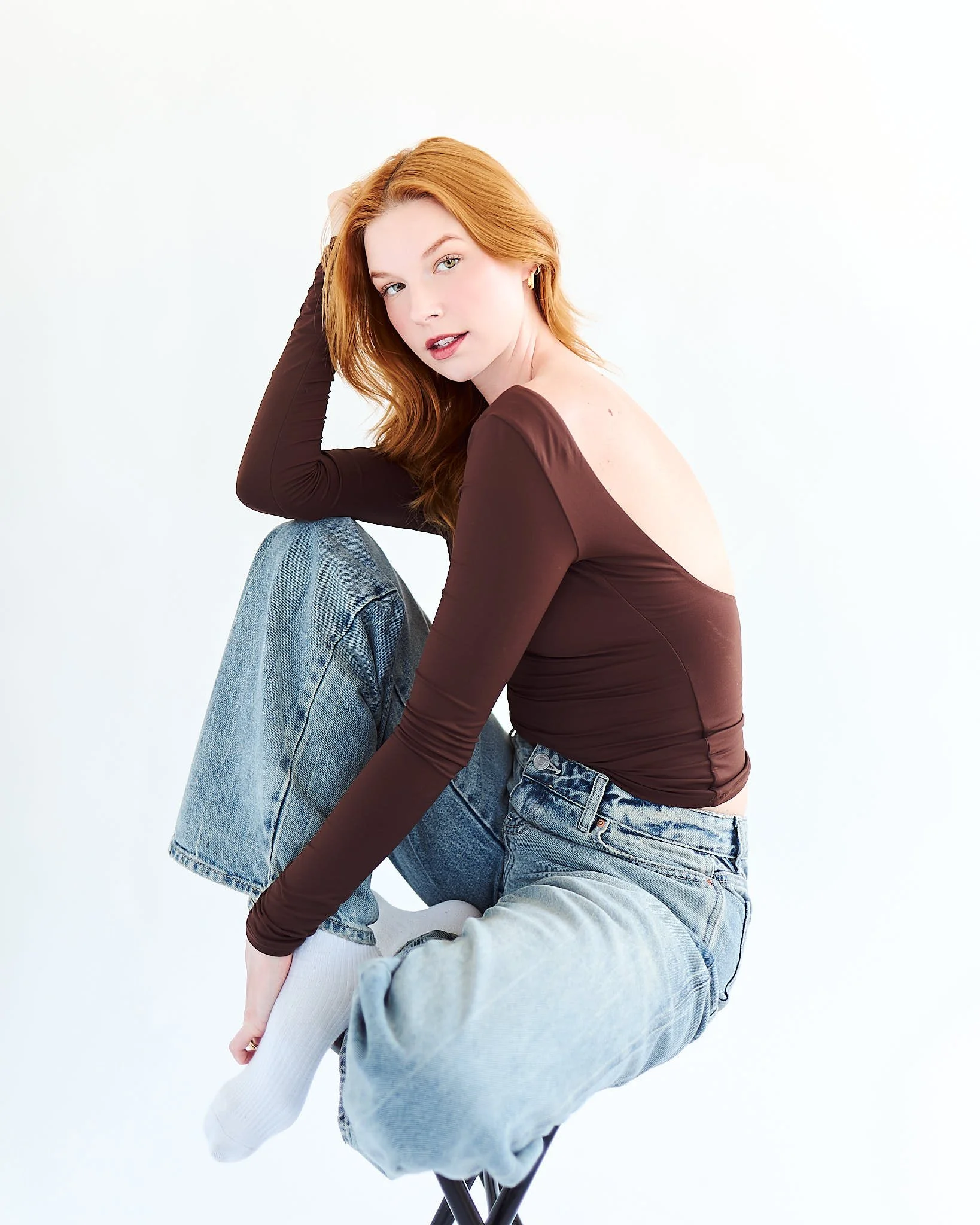 portrait of red head woman in front of off white backdrop sitting on a stool for her model development photography session in LA California