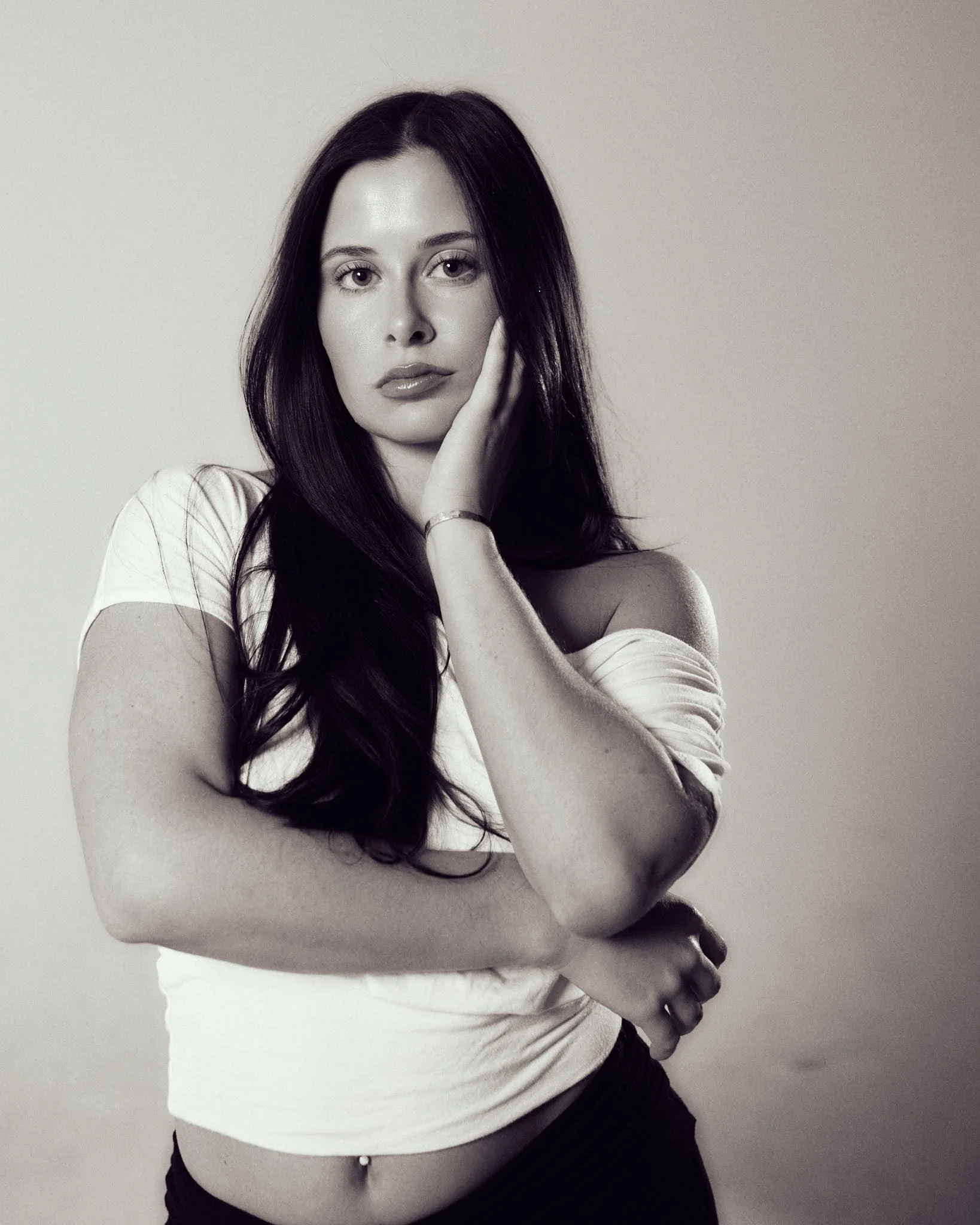 Black-and-white studio portrait of female model posing with hand against her face for model portfolio development.