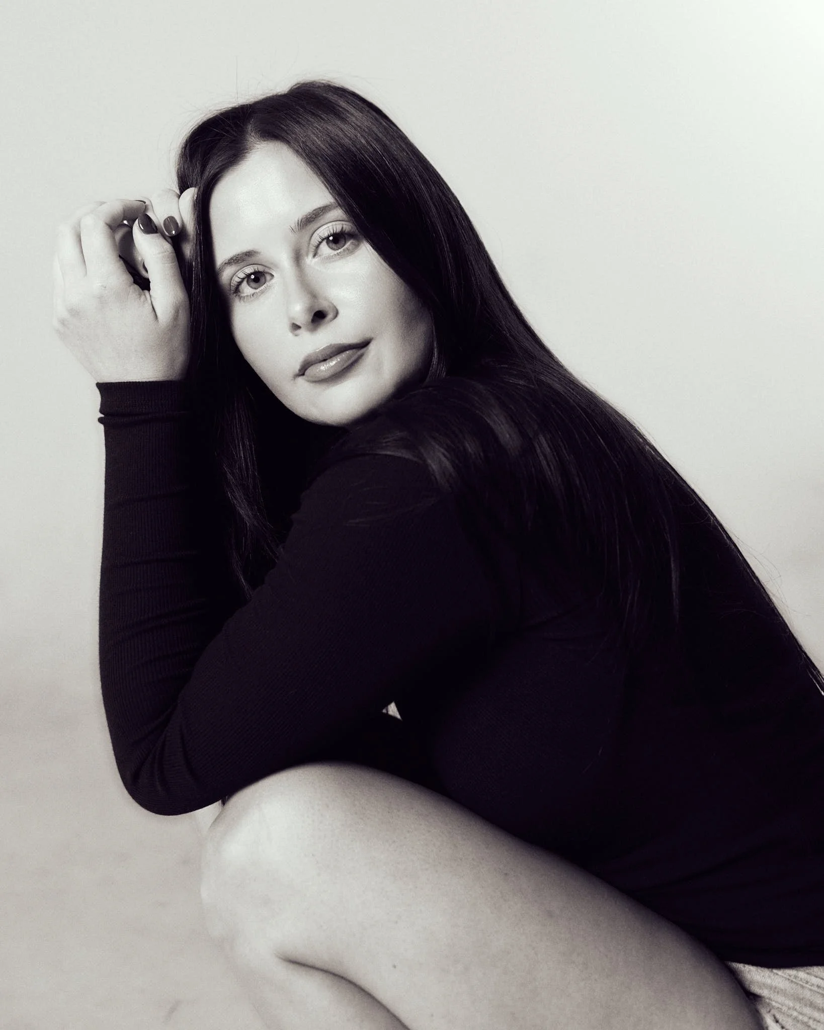 Black-and-white model development portrait of female model seated in a black long-sleeve look.