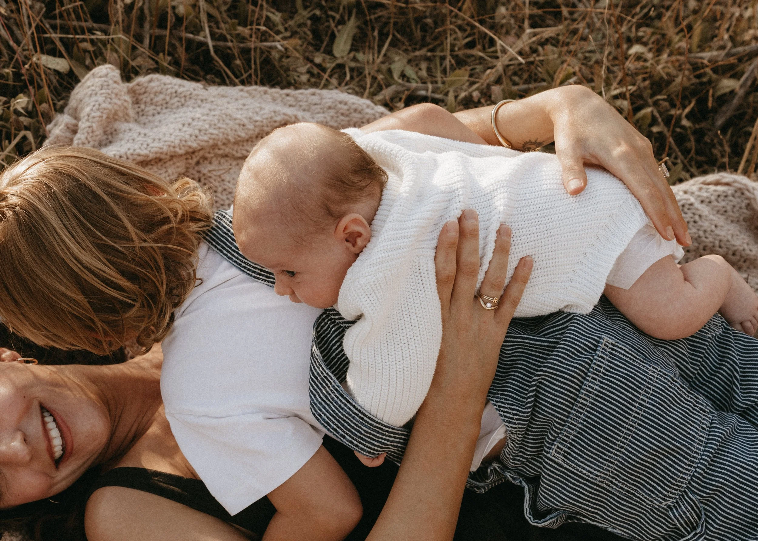 Warm family portrait of a mother and her two young boys lying together in a golden grassy field. 