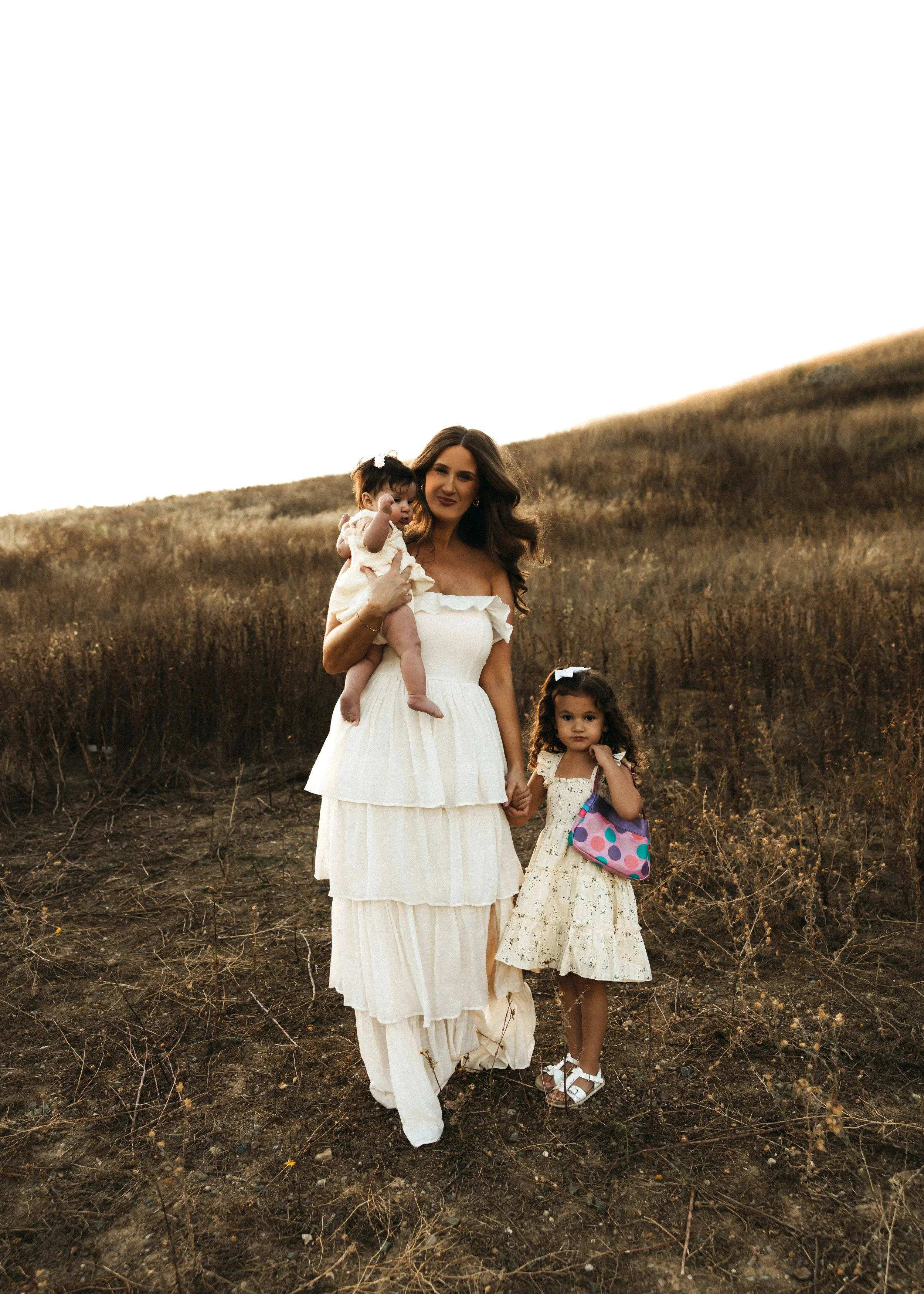 Mother standing with her two children in a golden field, styled in soft neutral outfits from a client closet.
