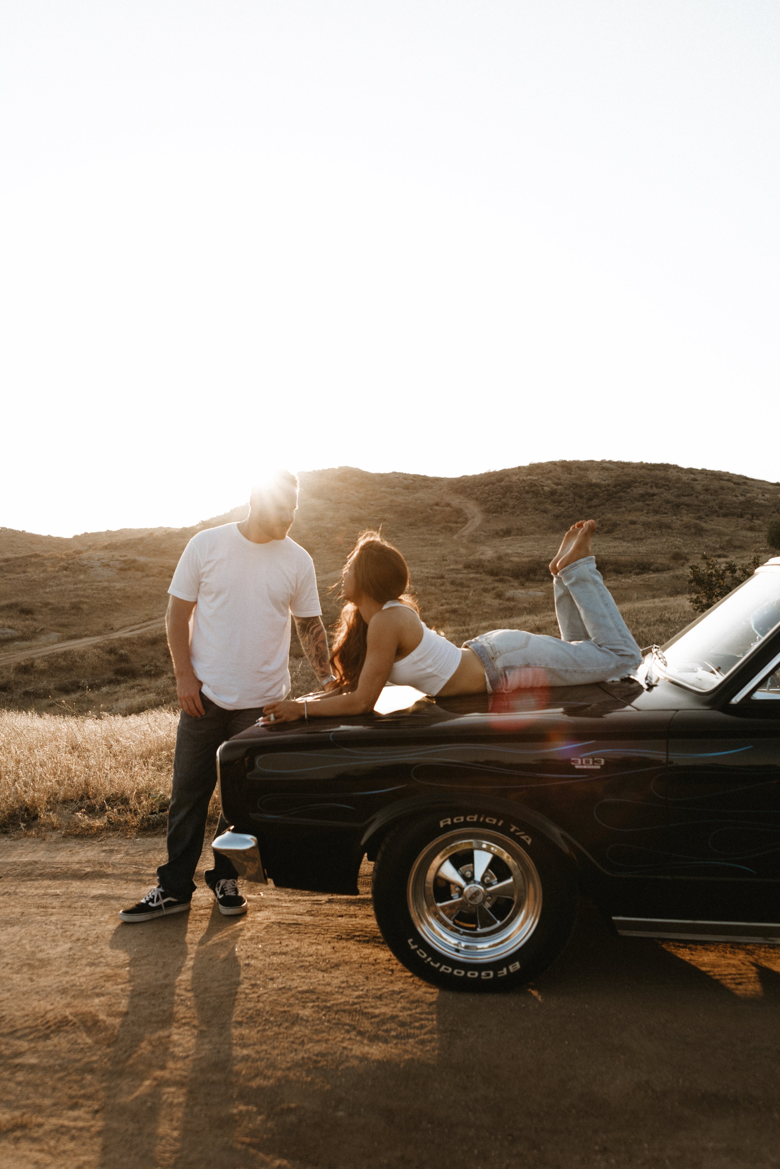 Couple posing on a vintage car in a golden outdoor landscape.