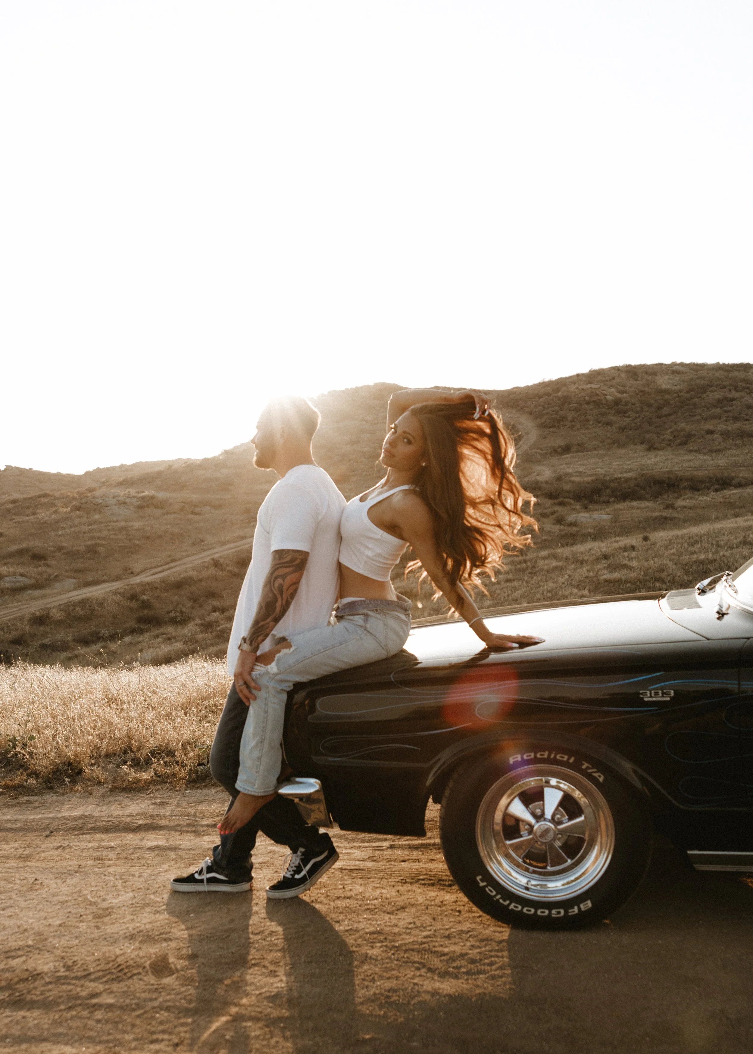 Couple posing on the hood of a vintage car in warm golden-hour light.