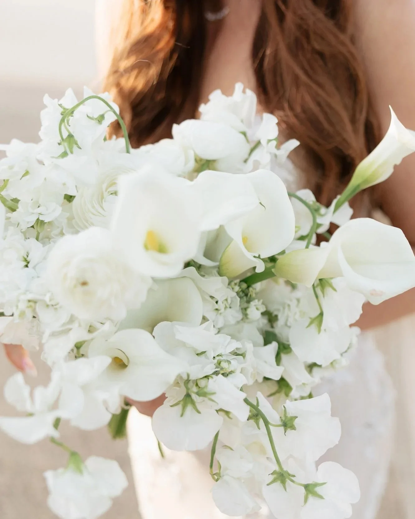 Close-up wedding detail photo of a white bridal bouquet with soft floral texture and bridal gown details.