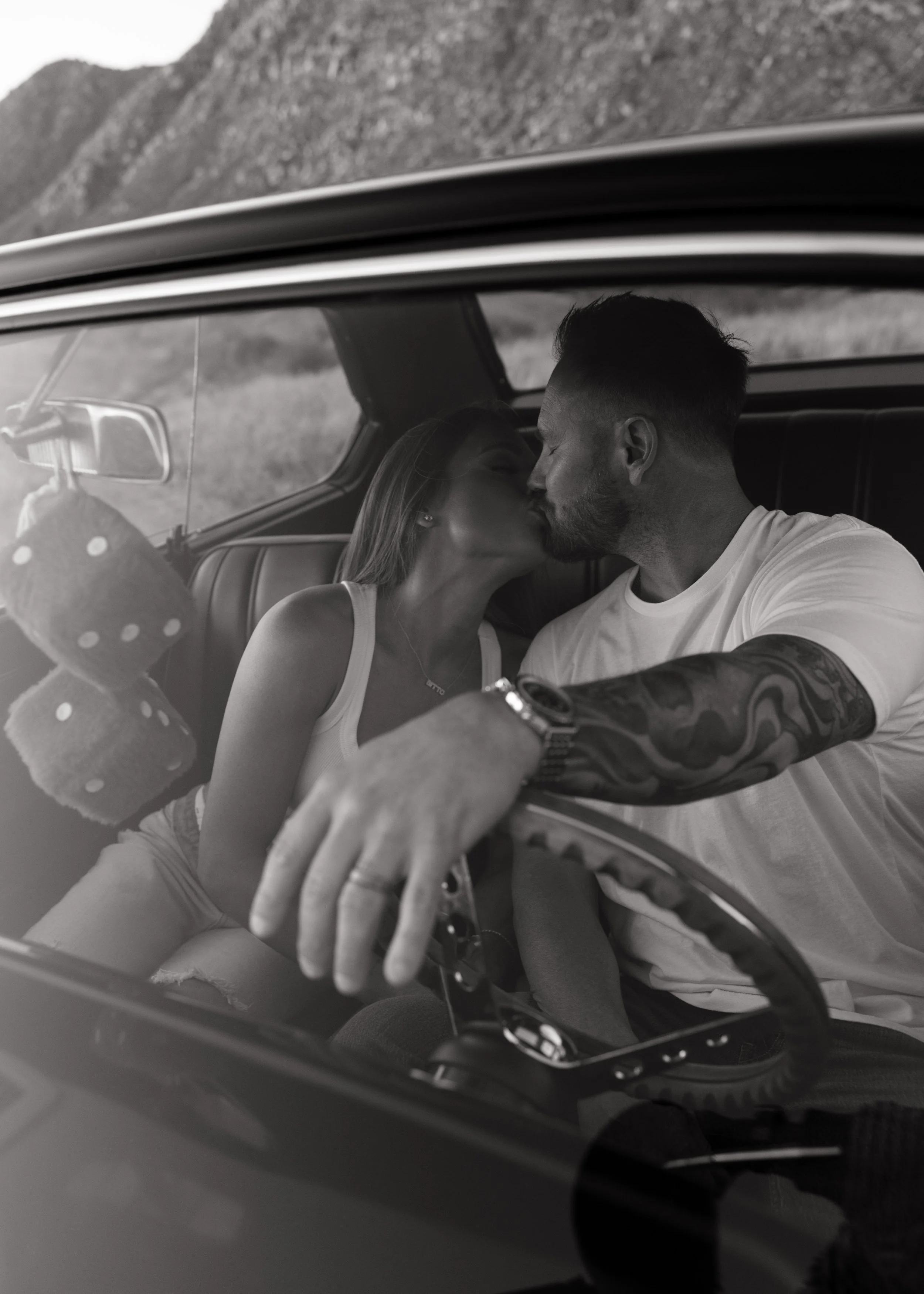Black-and-white candid photo of a couple sitting together inside a vintage car.