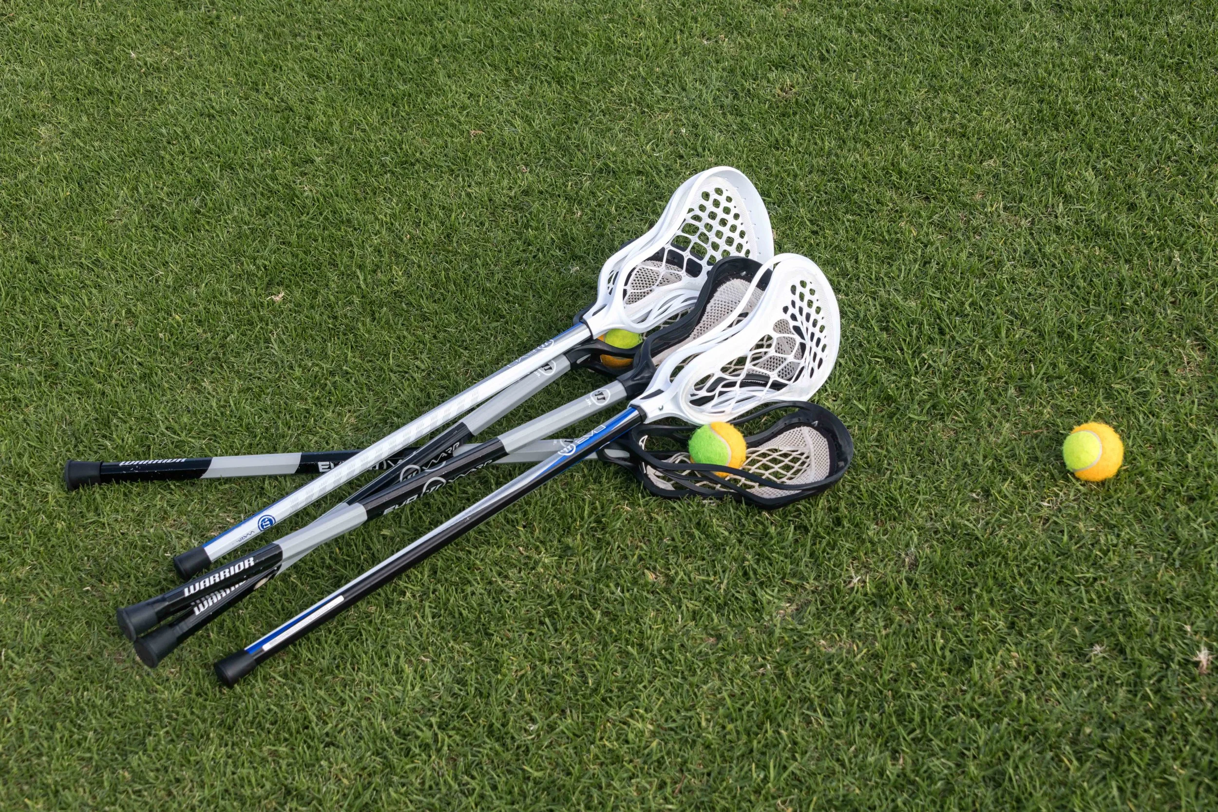 Three lacrosse sticks with yellow and green tennis balls on green grass.