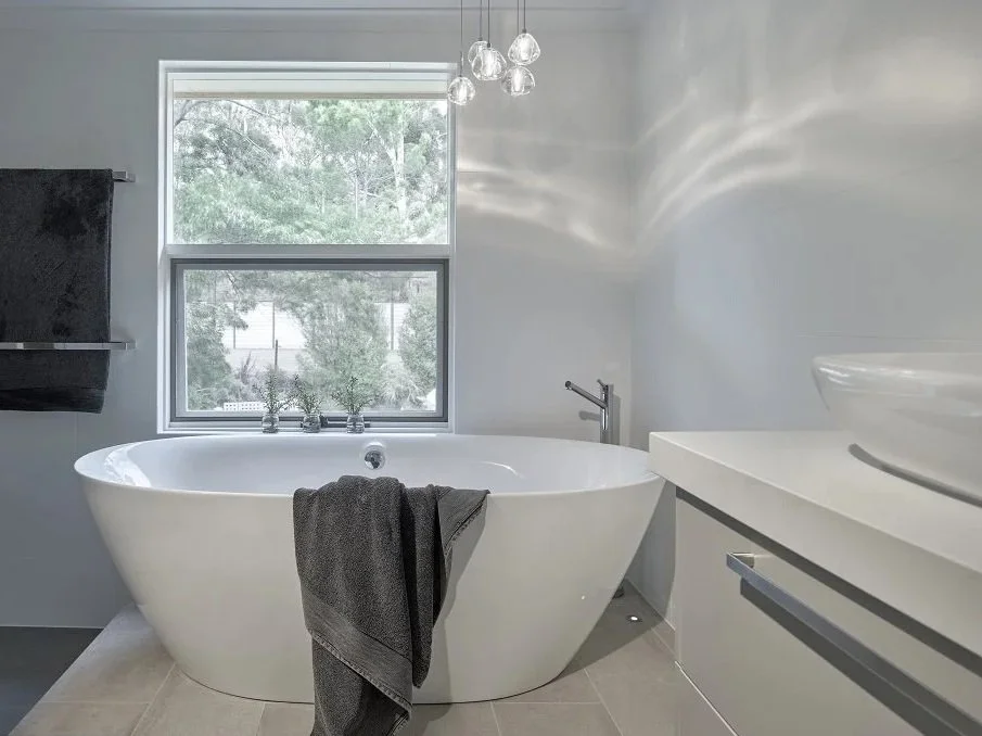Modern bathroom with a raised freestanding bath illuminated with hanging glass pendant lights.