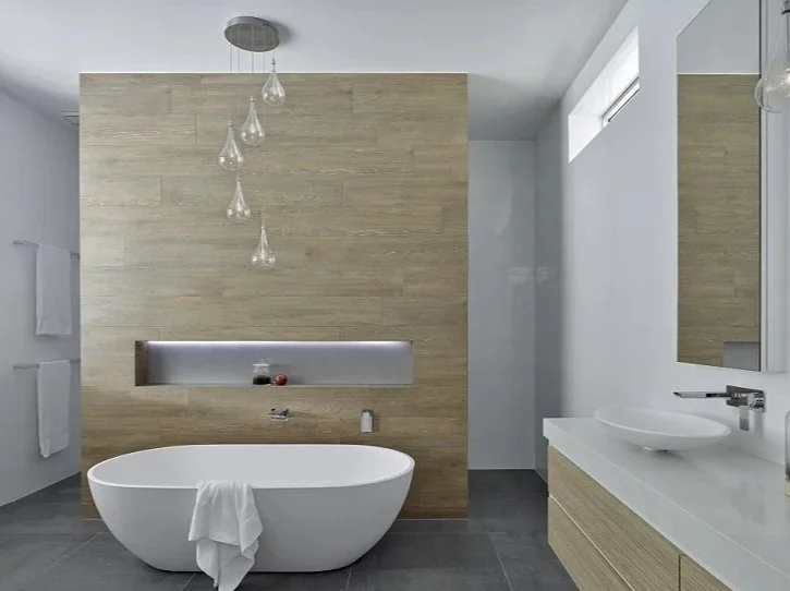 Modern bathroom with freestanding bathtub, wooden accent wall, wall-mounted sink, and pendant lights.