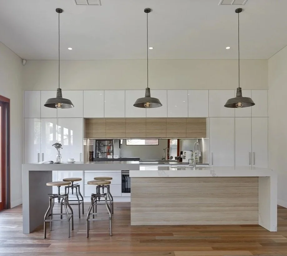 Modern kitchen with white cabinets, wooden accents, three hanging pendant lights, a kitchen island with seating, and hardwood flooring.