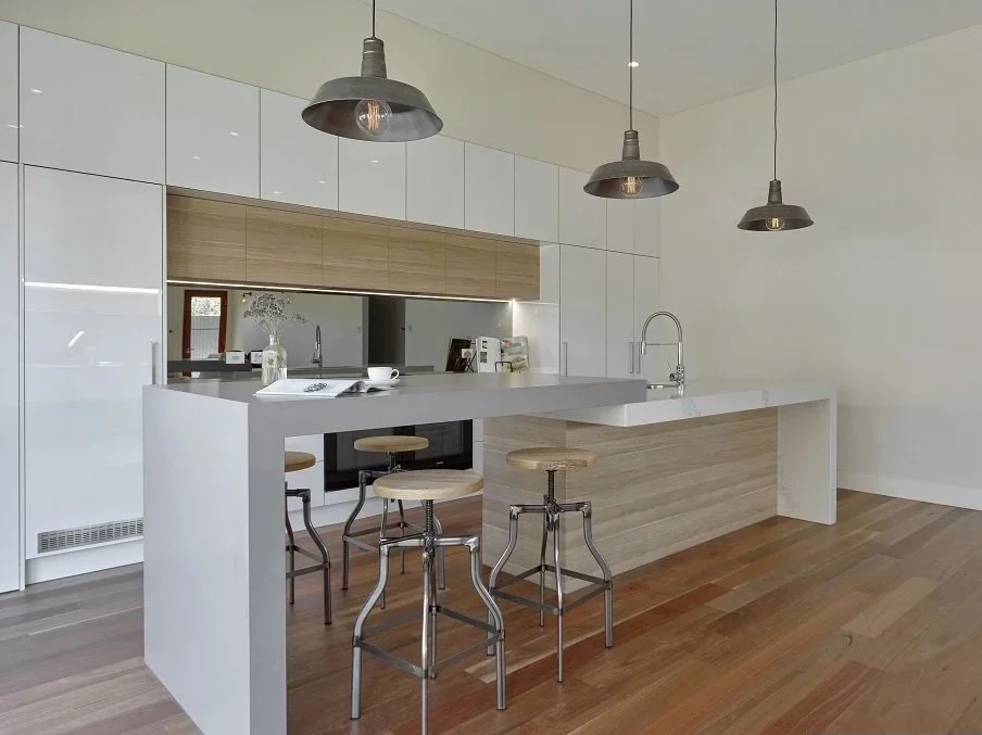 Modern kitchen with white cabinets, a white island, pendant lights, wooden bar stools, and a hardwood floor.