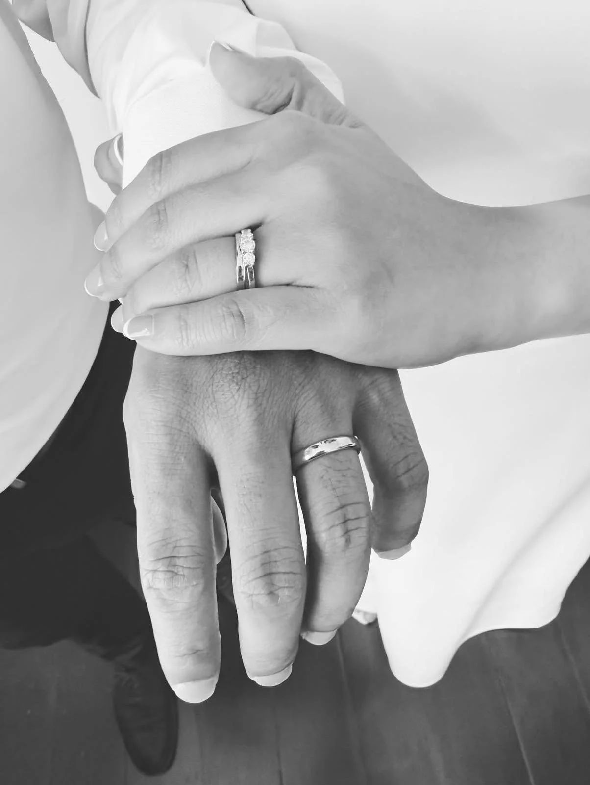 Close-up of two hands with wedding rings, one hand resting on top of the other, against a plain background.
