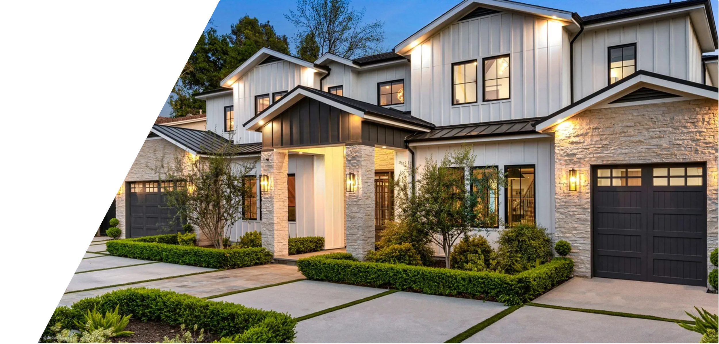 Modern multi-story house with black garage doors, stone accents, and white siding, surrounded by well-maintained lawn and bushes, illuminated by exterior lighting at dusk.
