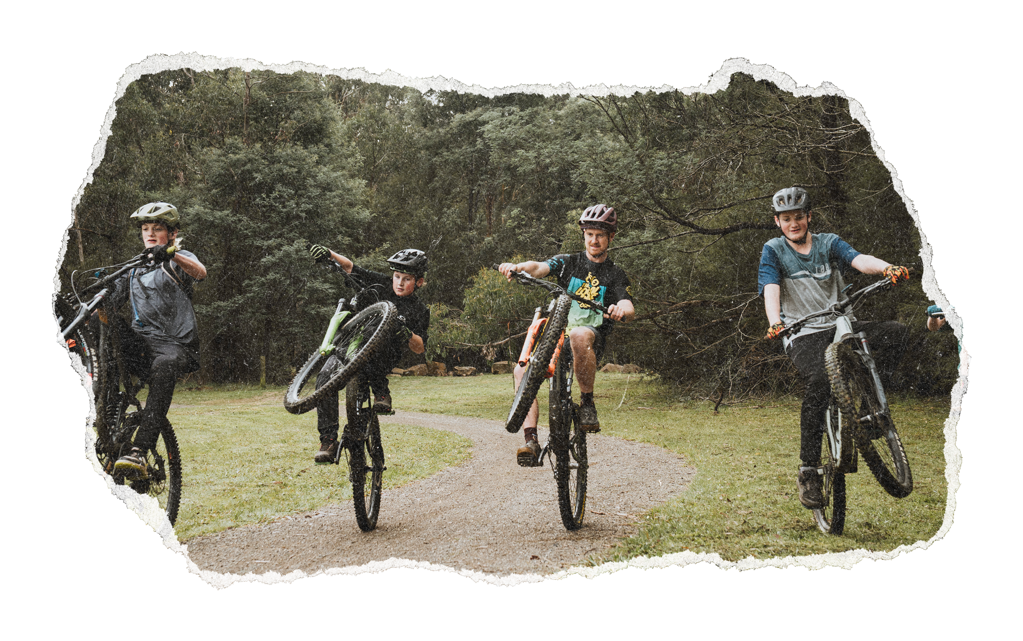 Four boys riding bikes on a dirt path in a wooded park, wearing helmets and casual clothes.