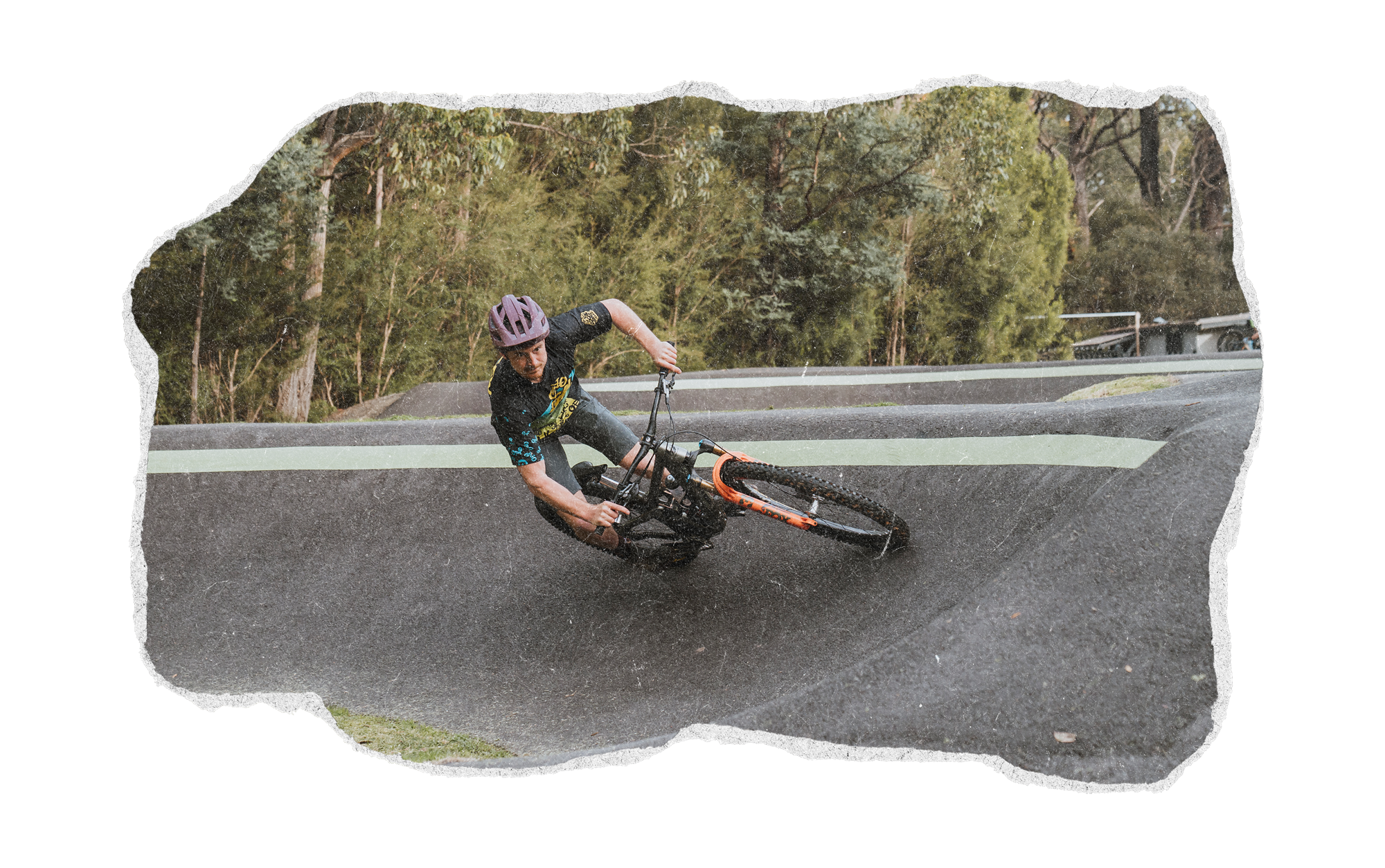 Person wearing a purple helmet riding a mountain bike on a wet, curving road surrounded by trees.