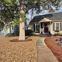 A house with a front porch, surrounded by a well-maintained yard with a large tree, mulch, and a curved walkway.
