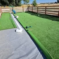 Child playing with a water slide on a backyard lawn with fence.