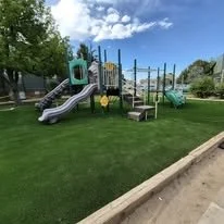 Colorful playground with slides, climbing structures, and swings on a grassy area under a blue sky.