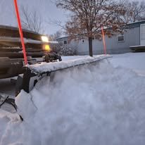 A snowblower clearing a driveway during winter, with snow being ejected from the machine.