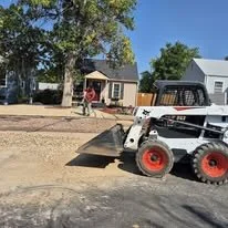 Construction site with a small bobcat loader on the street, and children playing near a swing set in the background.