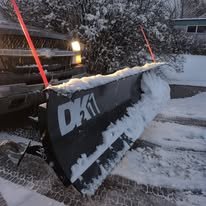 Snowplow clearing snow from a parking lot with a large snowplow blade.