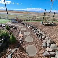 Stone pathway with large round stepping stones in a garden with a rural landscape in the background.