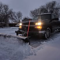 Black van with snowplow attachment clearing snow from a snowy road in winter