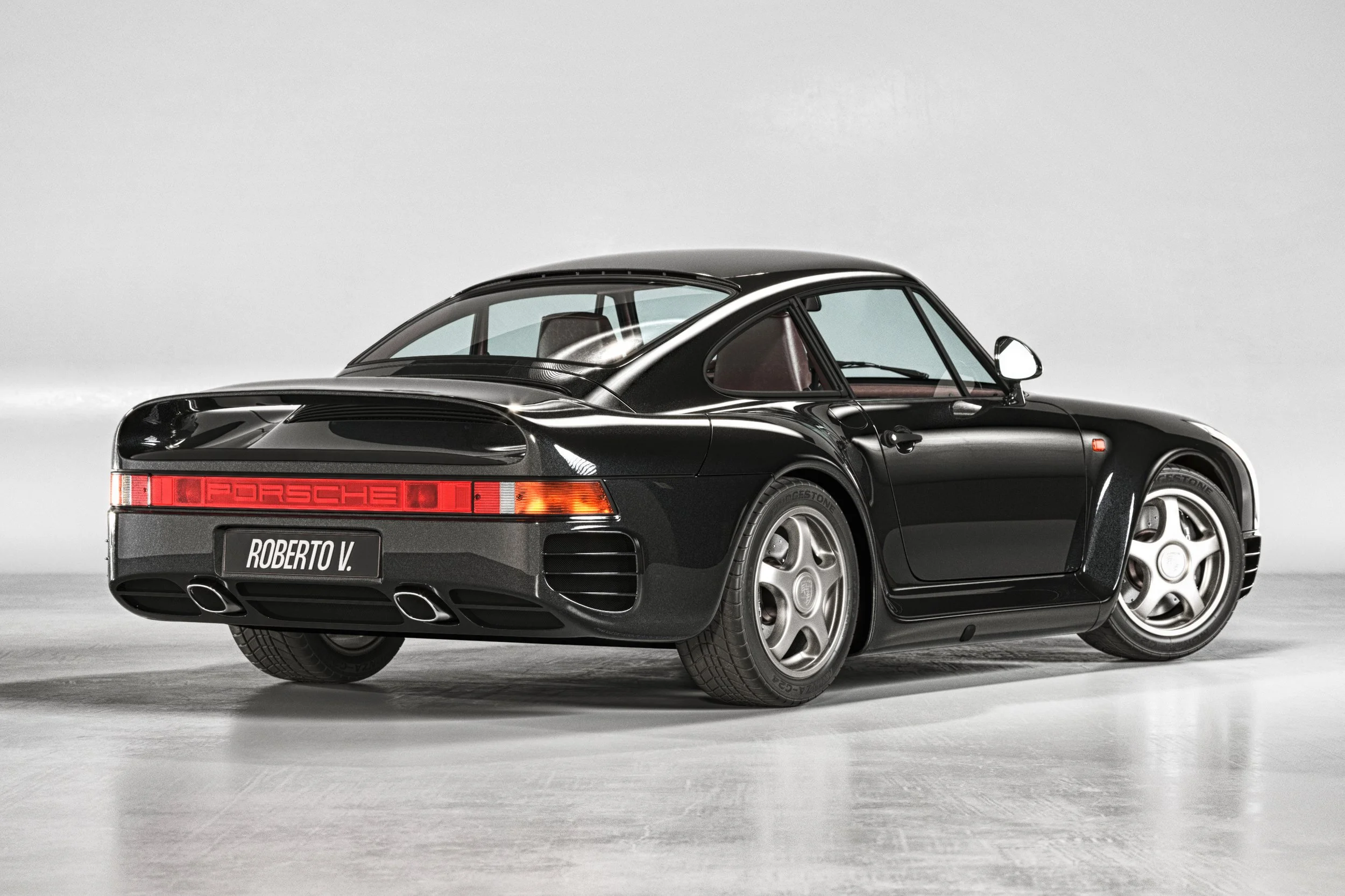 Photorealistic 3D car rendering of a Porsche 959 from a rear quarter view in a light gray studio, featuring realistic studio light reflections - Valenzuela Creative