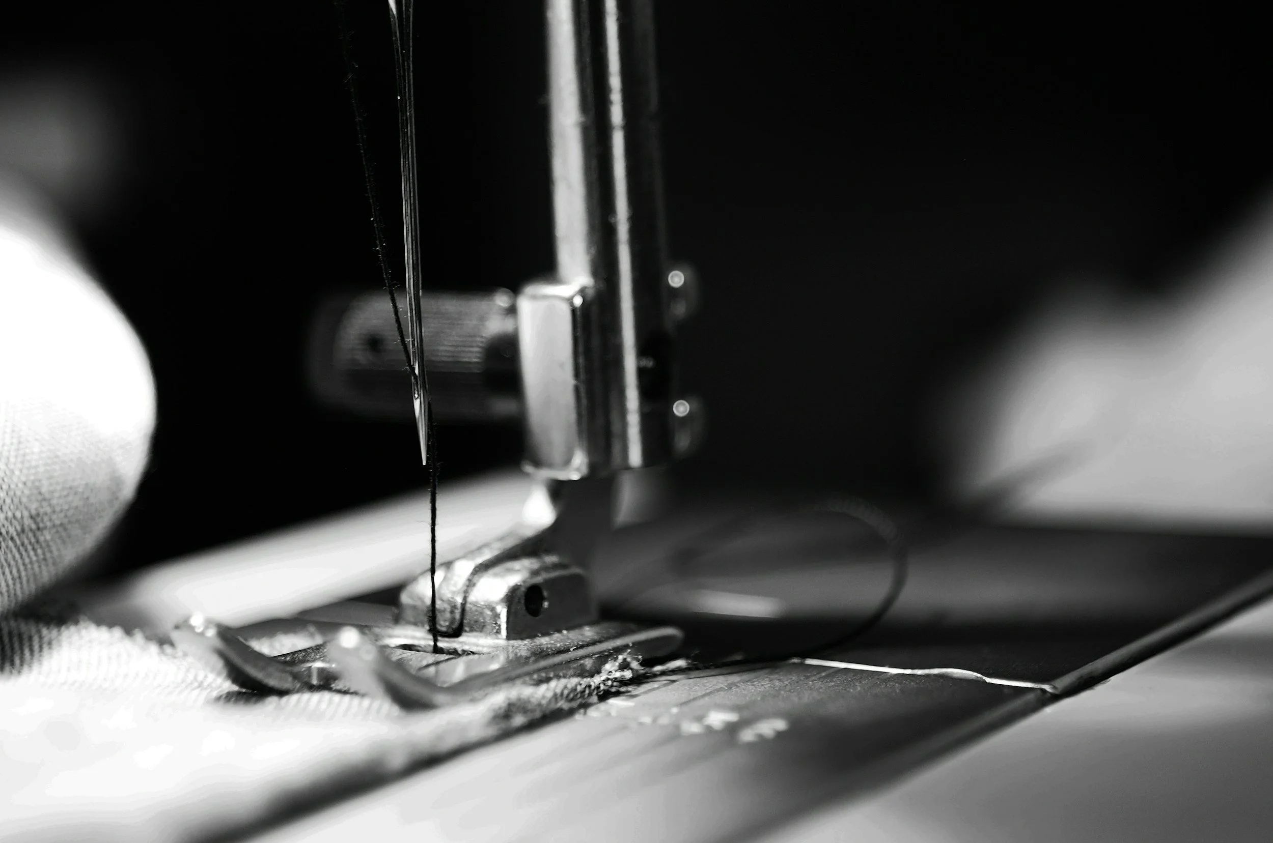 Close-up of a sewing machine needle and presser foot in action, stitching fabric in black and white.