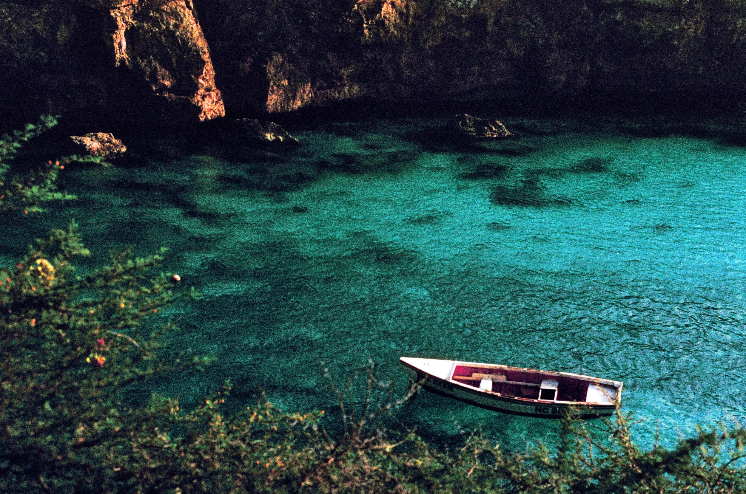 Nighttime scene of a boat docked near a rocky shoreline with dark, greenish water and a cave or cliff in the background.
