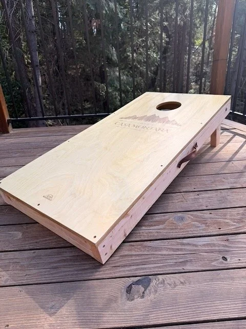 Regulation-size cornhole board propped on the deck at Casa Montaña, showing the frame construction and side profile against the property's forested backdrop.