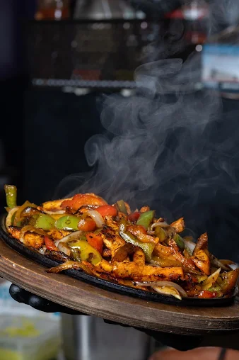 Colorful stir-fried vegetables served on a sizzling black skillet with steam rising.