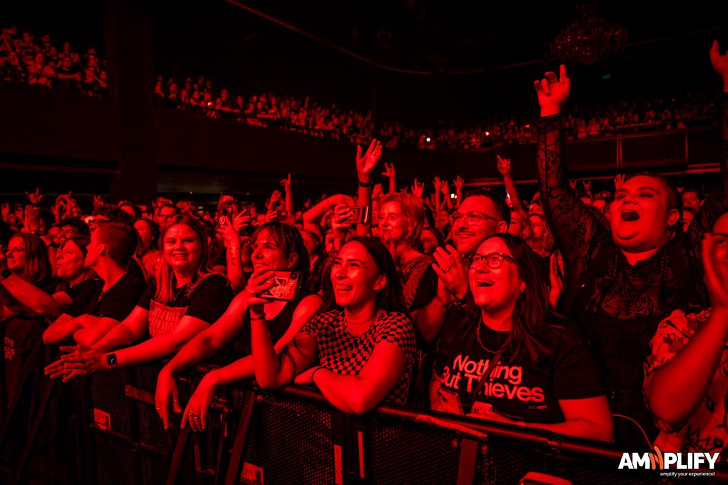 Audience at a concert or live event, enthusiastically cheering and enjoying the performance, illuminated by red stage lighting.
