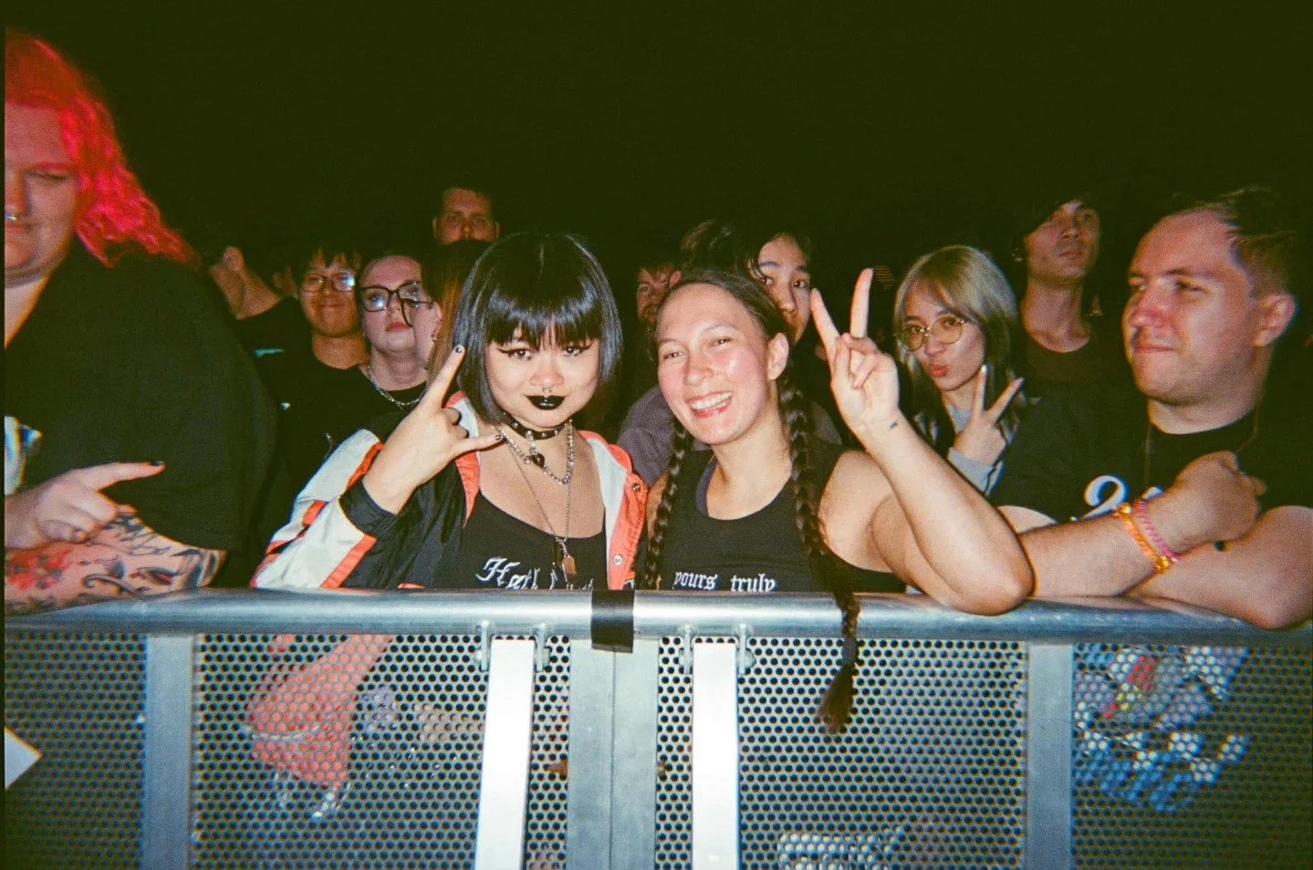 Group of young people at a concert, with two women in the front making peace signs.