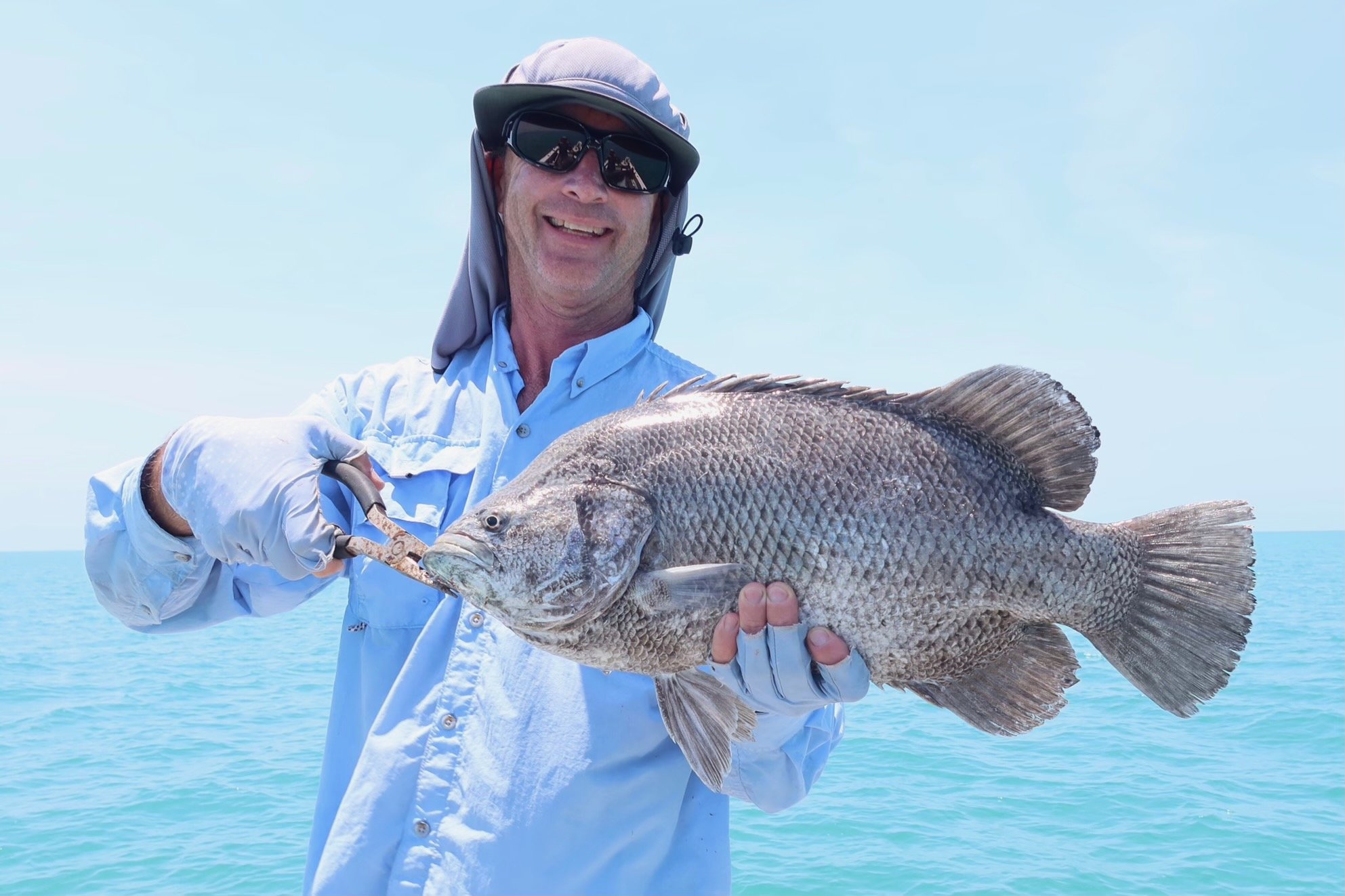 Local guide in fishing attire holding up triple tail fish.