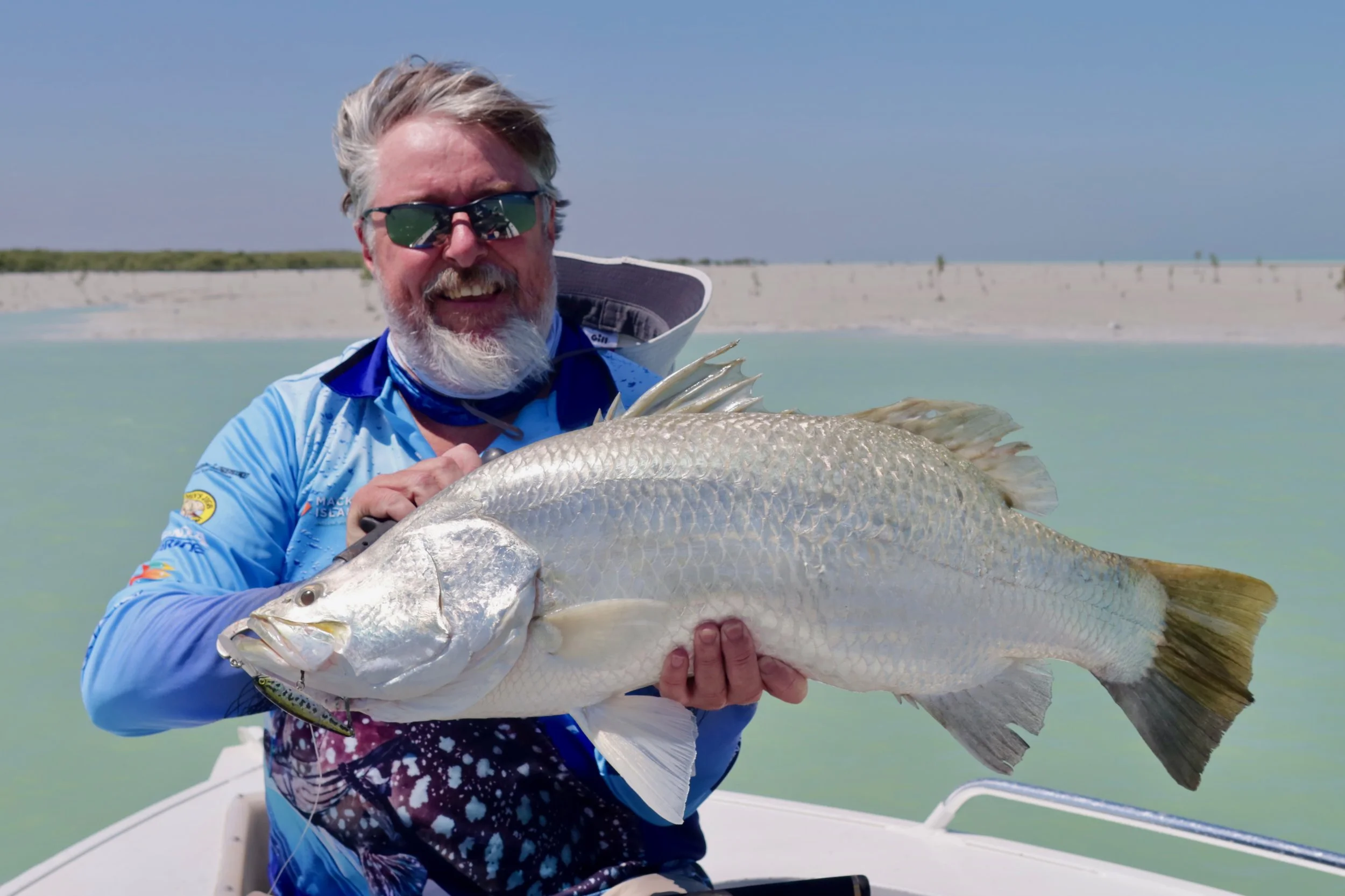 Fisherman holding a large barramundi with local creek in the background.