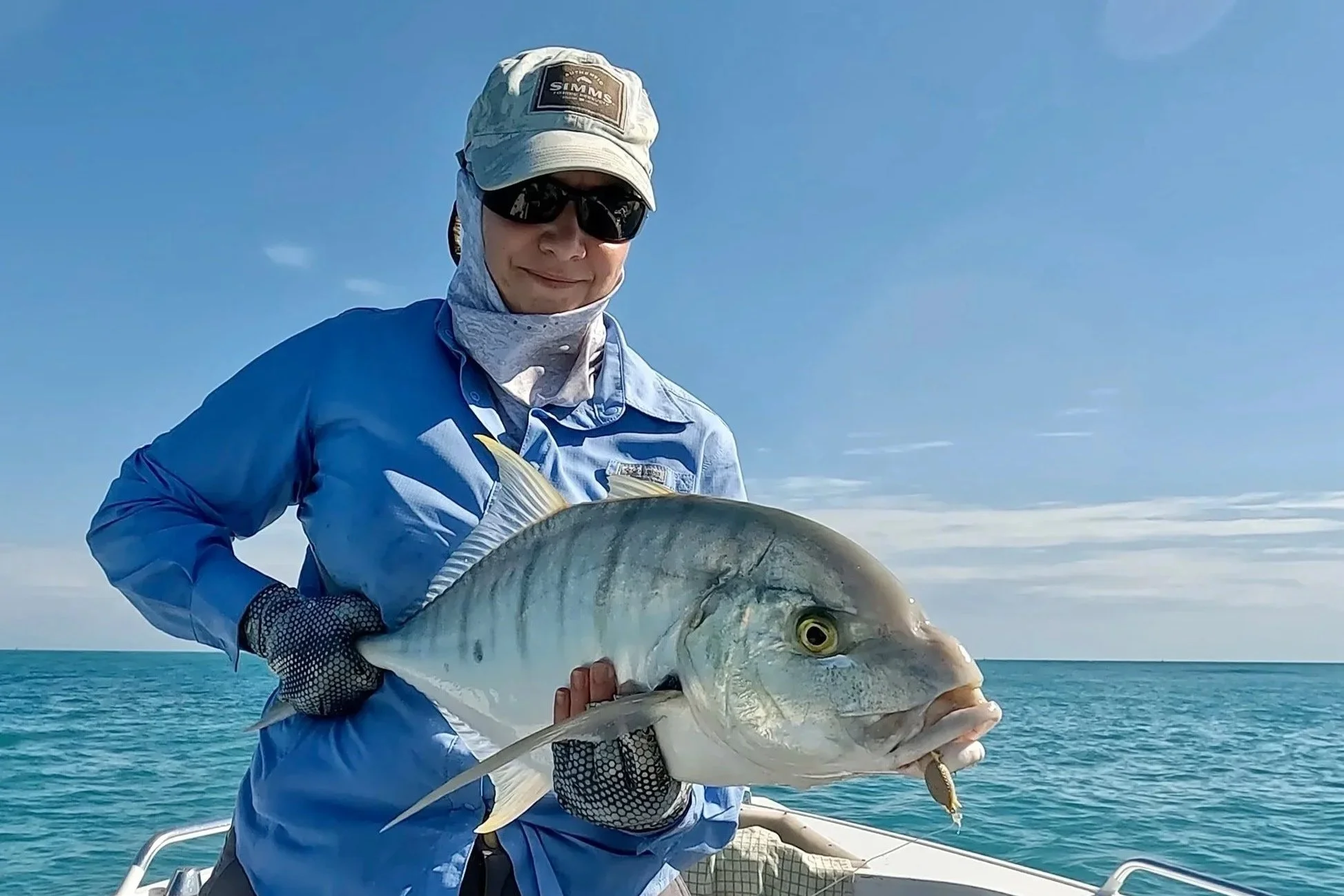Woman fishing, holding golden trevally.