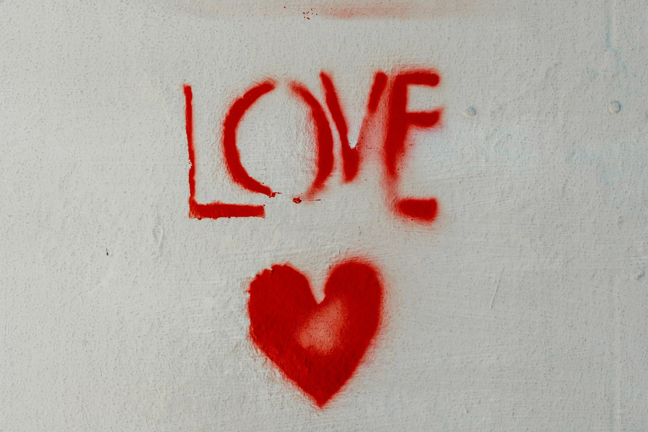 Red spray-painted graffiti on a wall forming the word 'LOVE' with a heart symbol underneath it.