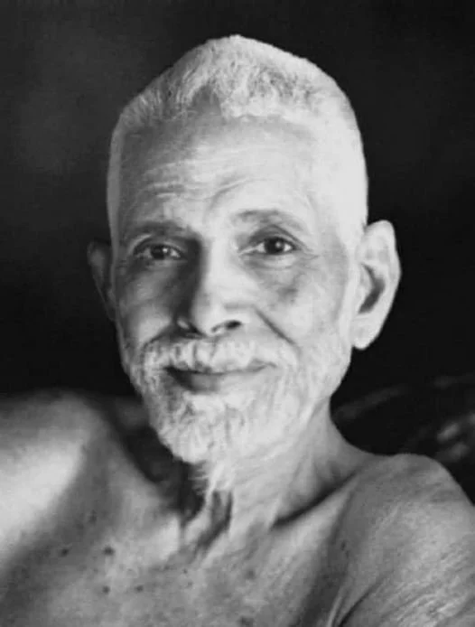Black and white photo of an elderly man with a short white beard and mustache, smiling, with short white hair, shirtless, against a dark background.