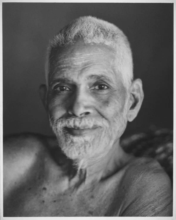 Black and white portrait of an elderly man with short gray hair and a beard, smiling slightly, shirtless against a plain background.
