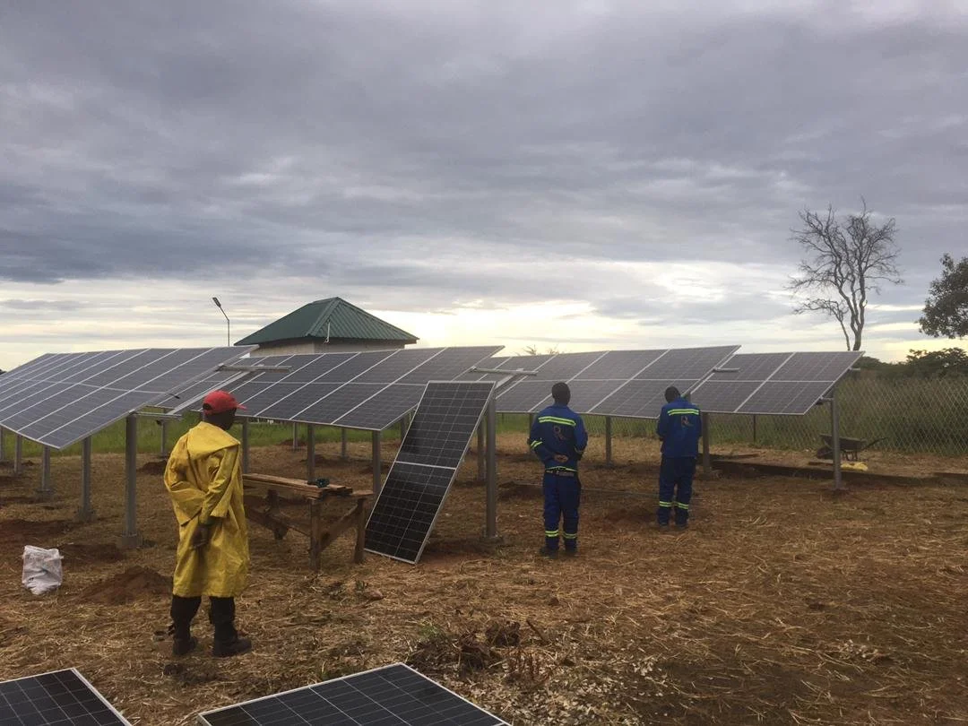 Three workers inspecting solar panels installed in an open field under cloudy sky.